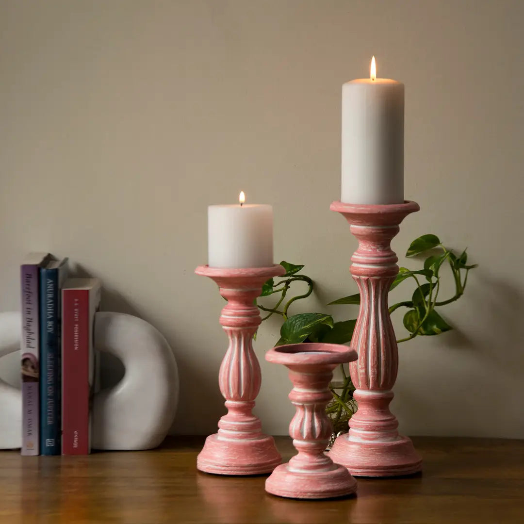 Pink sculptural candle holders with lit candles beside books and a ceramic accent, illustrating Calmly Elevated’s focus on scent and mood in interior spaces.
