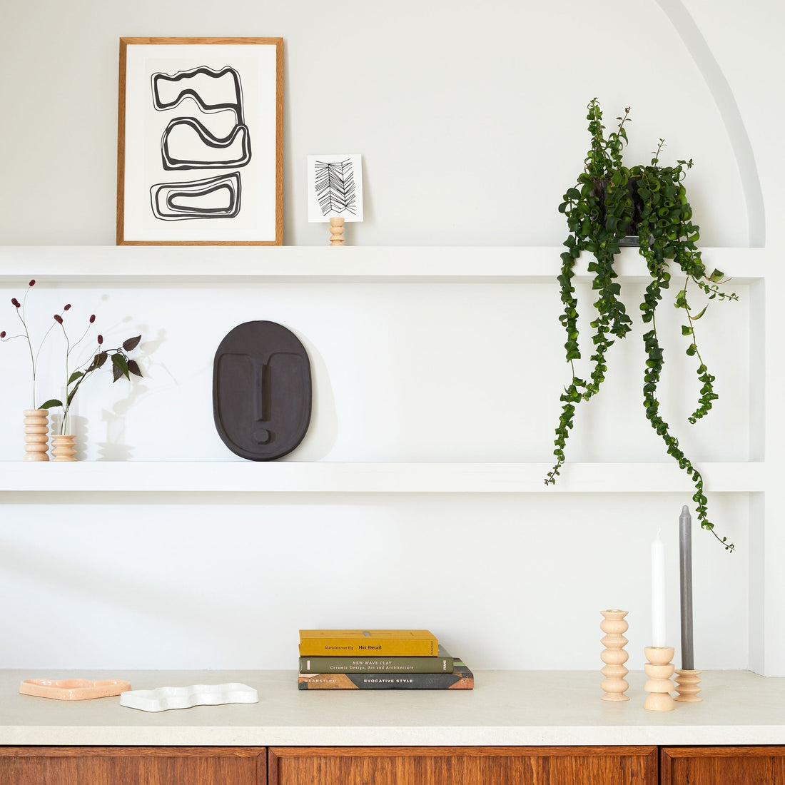 Minimalist white shelving with neutral ceramics, greenery, and abstract art, evoking calm and balance in interior design.