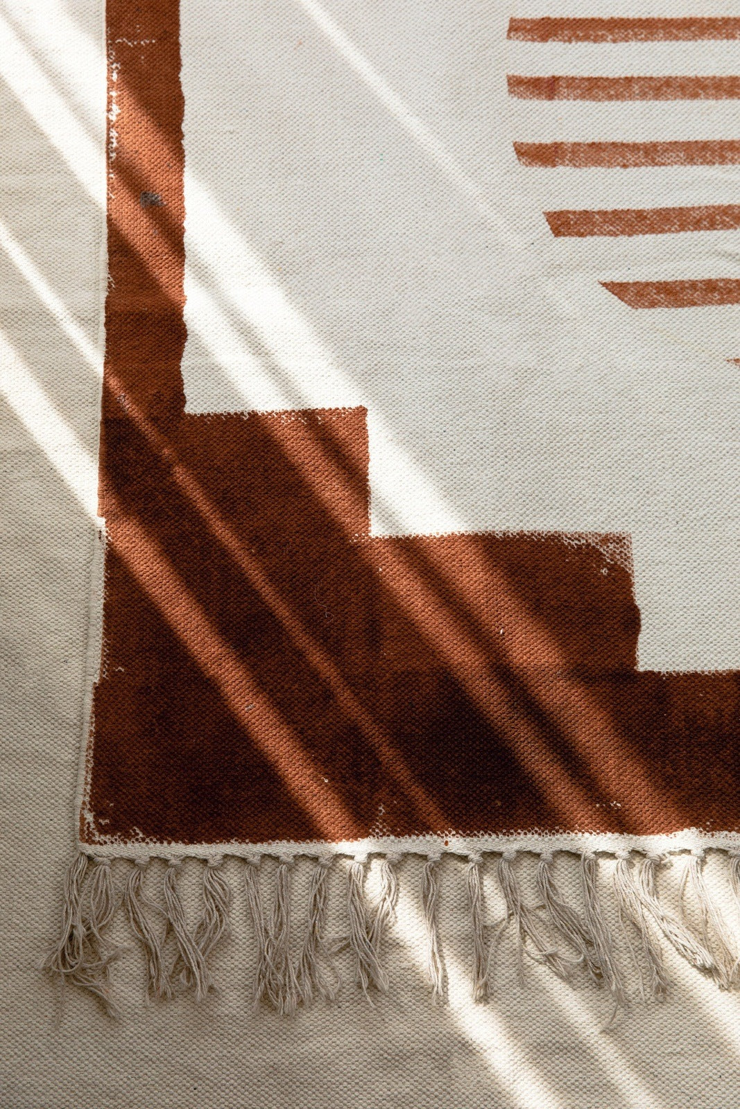 Natural sunlight and warm shadows on a terracotta and cream geometric rug, symbolizing how light and texture influence home energy