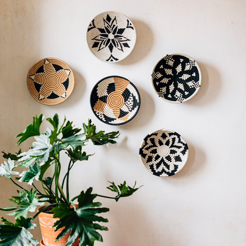 Handwoven decorative wall bowls and woven art pieces displayed on a white wall with plants