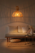 Aura rattan pendant light casting warm woven shadow patterns on a wall above a neutral linen daybed in an evening living room setting