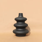 Black Mezo ceramic vase with stacked sculptural tiers on a warm tan backdrop