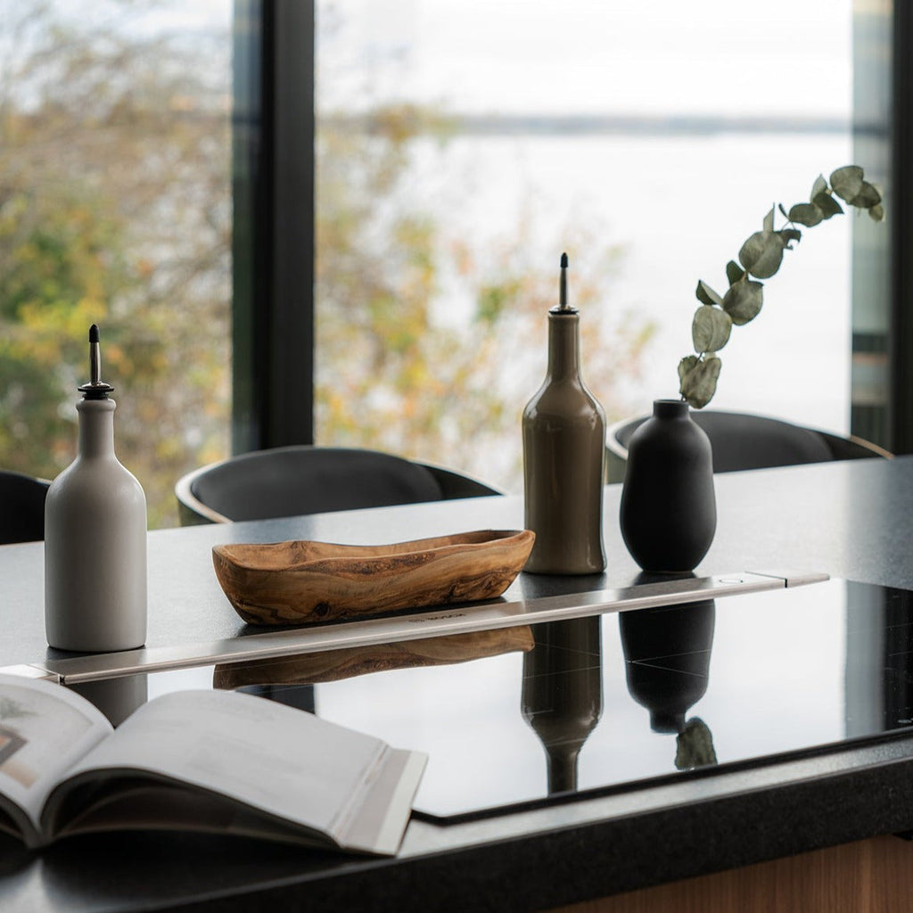 Black stoneware vase styled with oil bottles and a bowl on a window shelf