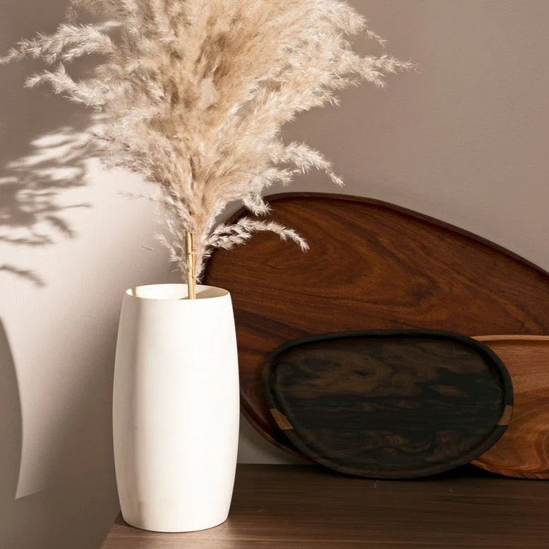 Hand finished Guatemalan wood vase holding pampas grass beside wooden boards