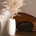 Hand finished Guatemalan wood vase holding pampas grass beside wooden boards