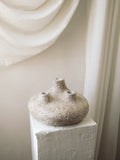 Handcrafted Amit Vessel with three spouts and a textured sandy terracotta finish on a white plaster pedestal