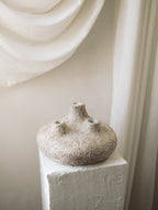 Handcrafted Amit Vessel with three spouts and a textured sandy terracotta finish on a white plaster pedestal