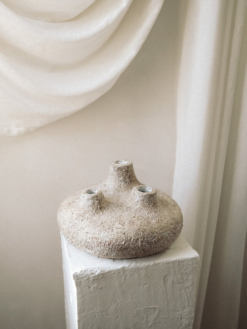 Handcrafted Amit Vessel with three spouts and a textured sandy terracotta finish on a white plaster pedestal