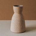 Handcrafted Reloj hourglass vase in raw terracotta on a stone surface against a warm backdrop