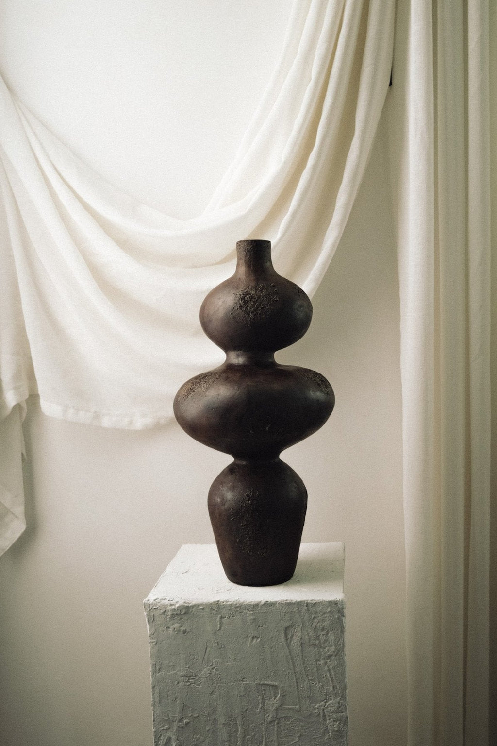 Handcrafted Sewu terracotta vessel with tiered curved form on a white plaster pedestal