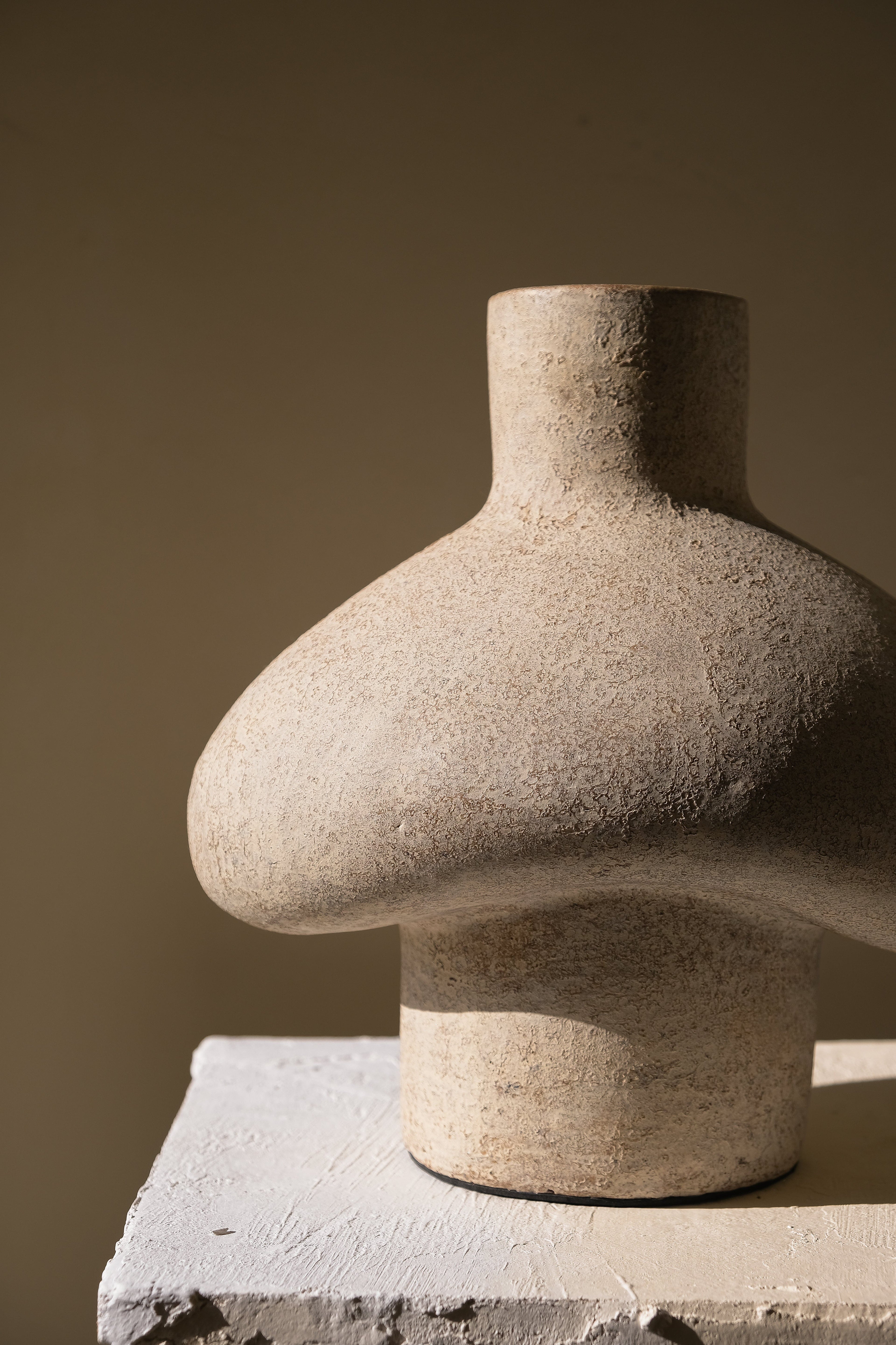 Side view of the textured shell white Tanah vessel on a plaster pedestal