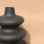 Matte black Mezo vase showing its curved tiered contour against tan