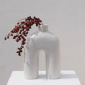 Off white Ozo ceramic arch vase holding a draping red berry branch on a white plinth