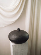 Rovi disc-shaped terracotta vessel on a pedestal against soft draped linen