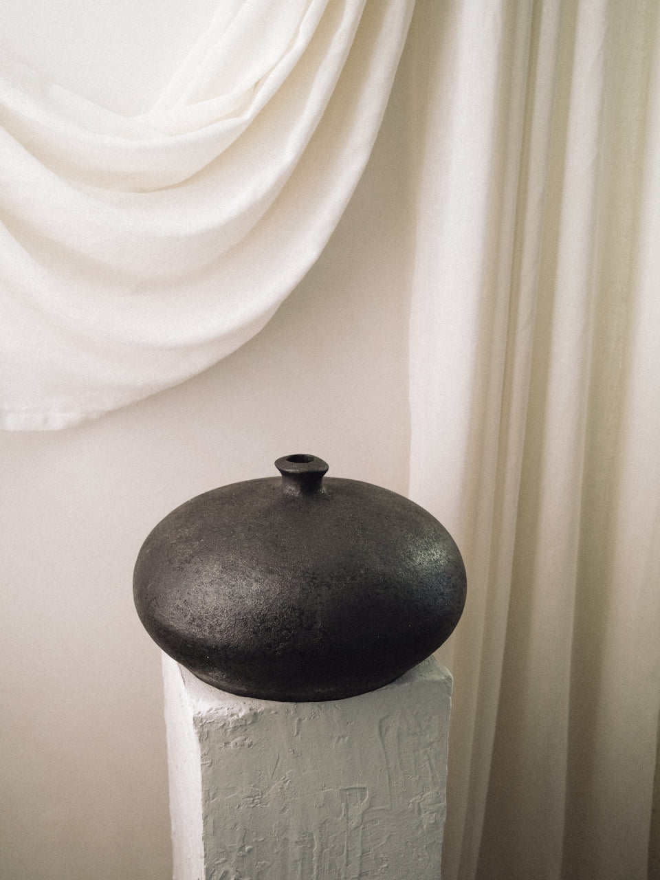 Rovi disc-shaped terracotta vessel on a pedestal against soft draped linen