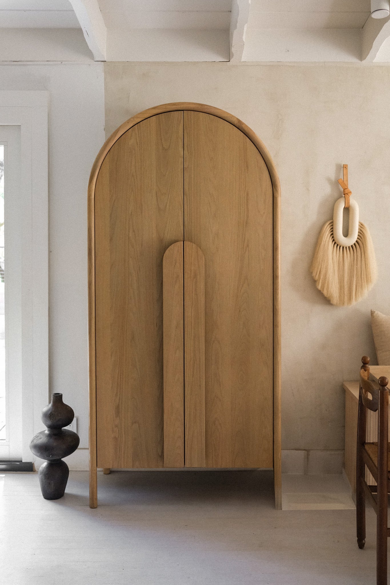 Sculptural terracotta vessel anchoring a corner near a curved wood arch entryway