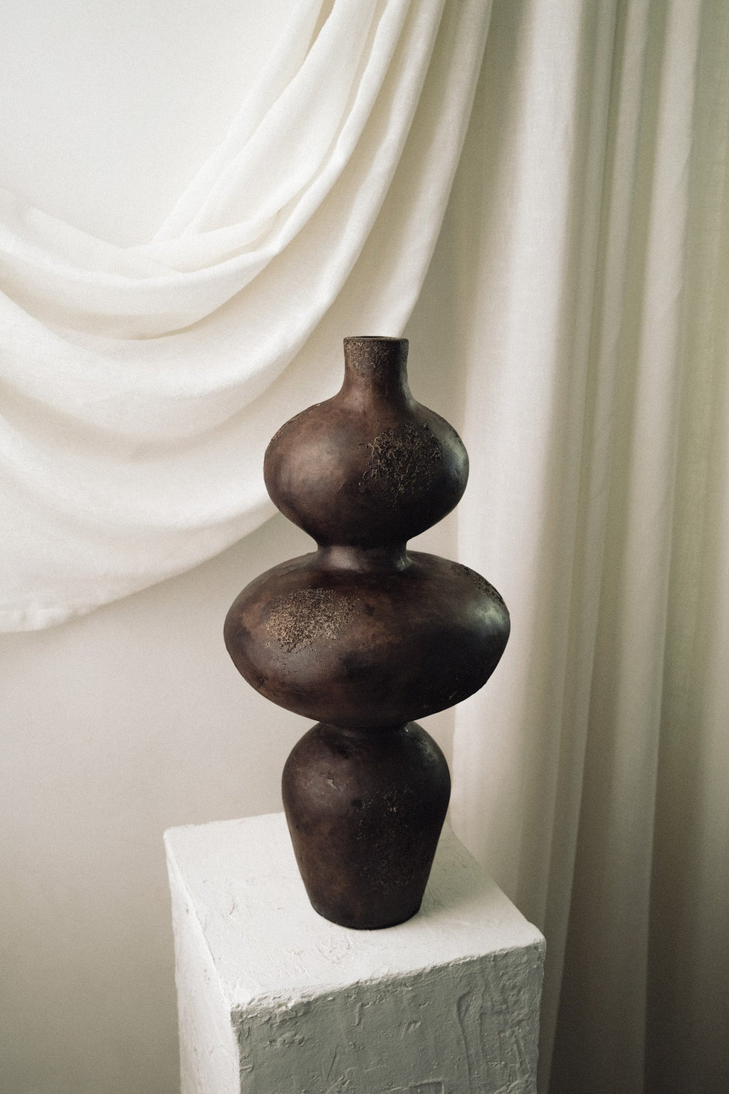 Sewu terracotta vase displayed on white pedestal against a draped linen backdrop