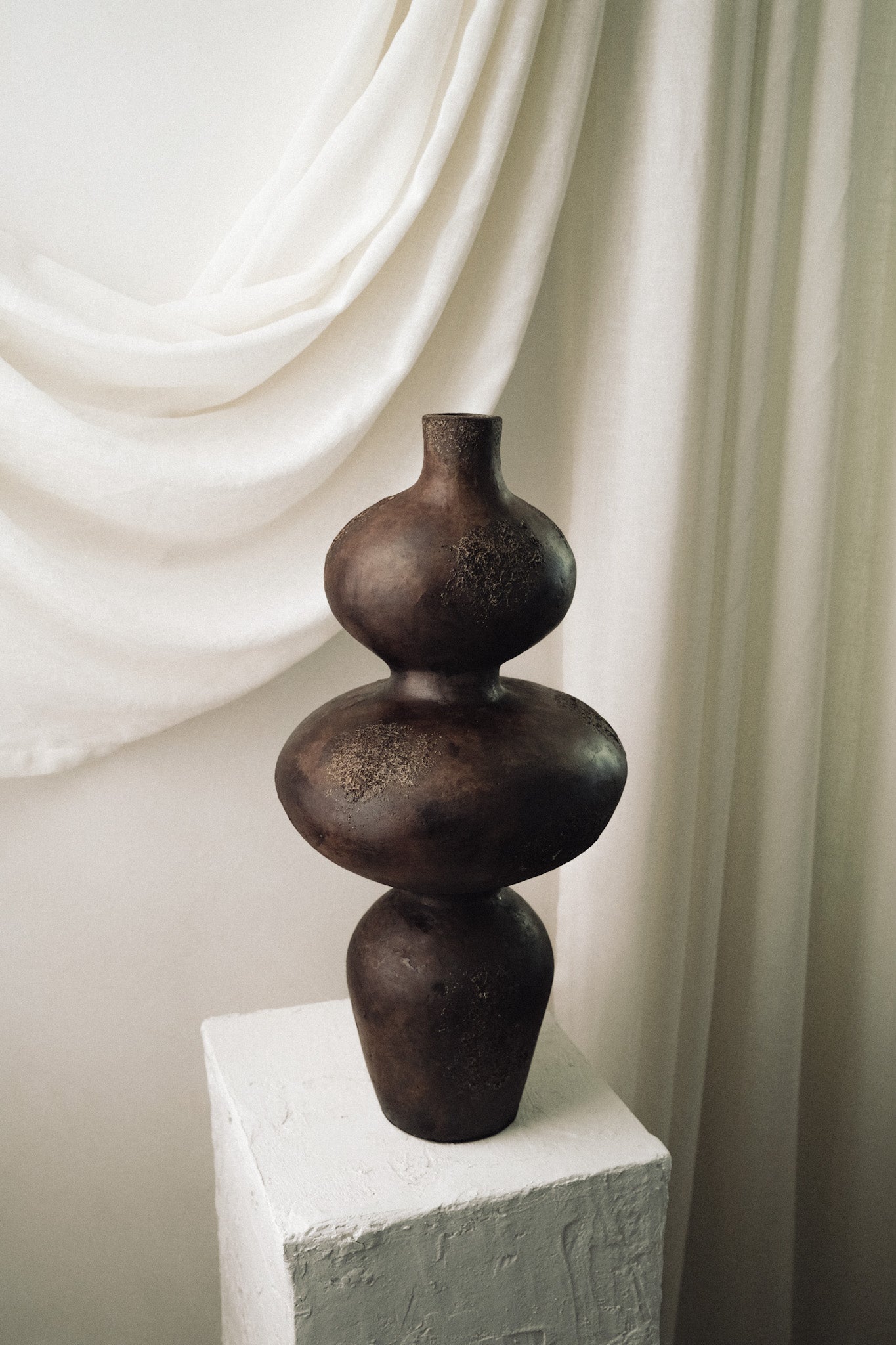 Sewu terracotta vase displayed on white pedestal against a draped linen backdrop
