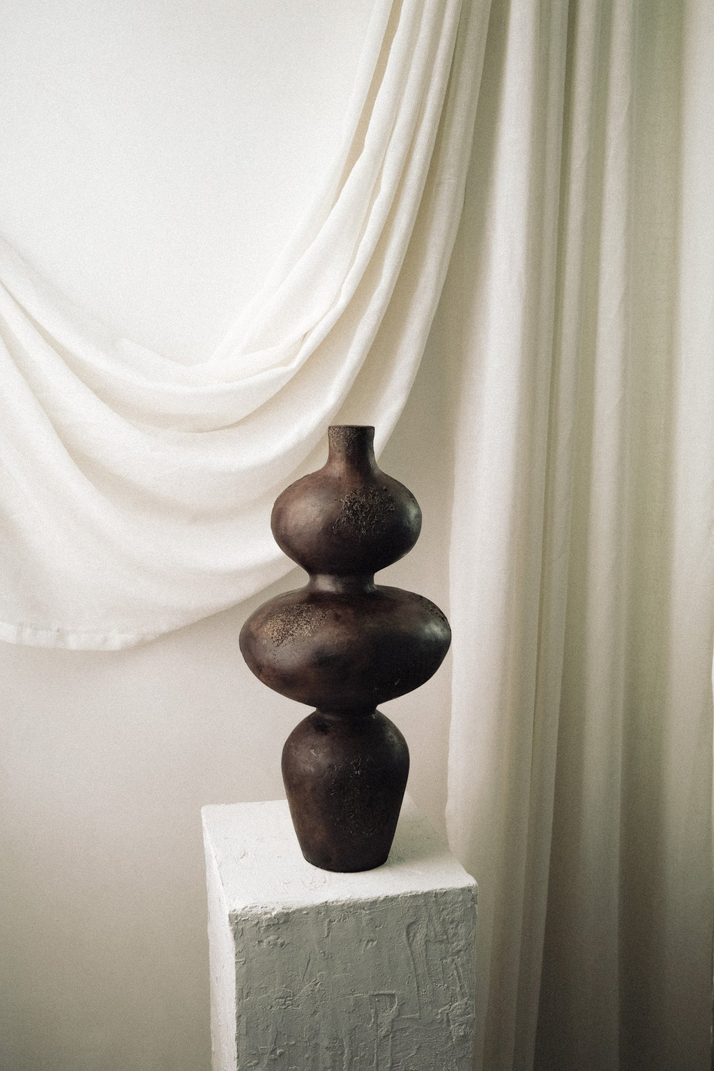 Side profile of the Sewu terracotta vessel against soft white drapery