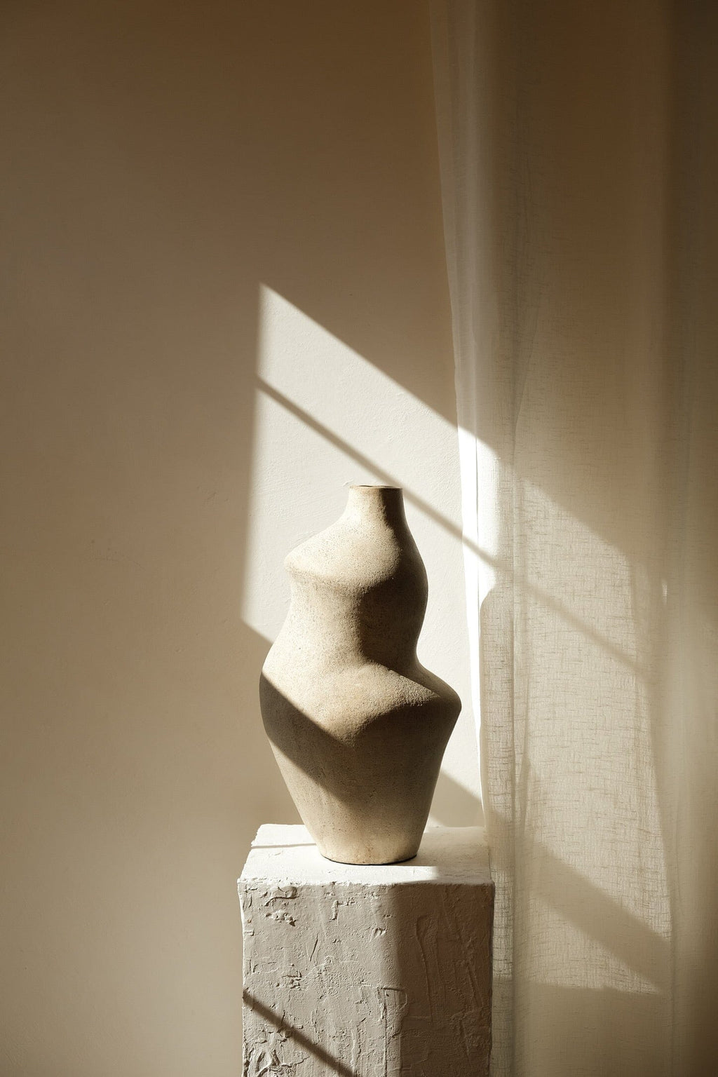 Suma cream terracotta vessel on a plaster pedestal in soft directional sunlight