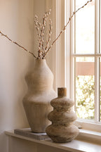 Suma terracotta vessel with budding stems grouped beside a window on a console
