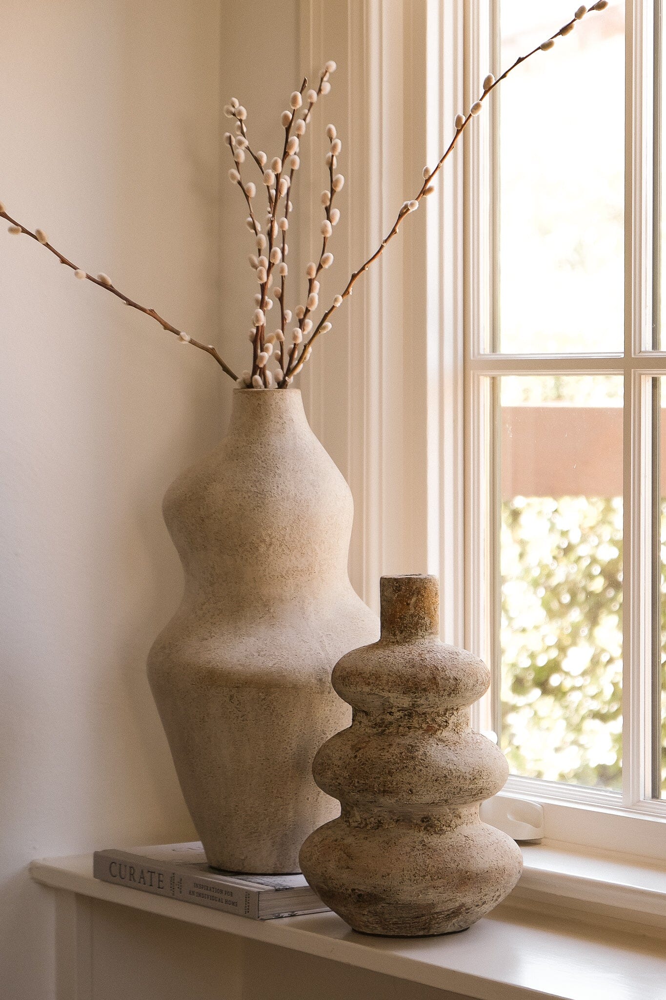 Suma terracotta vessel with budding stems grouped beside a window on a console