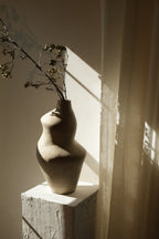 Suma vessel holding a tall budding branch on a plaster pedestal against draped linen