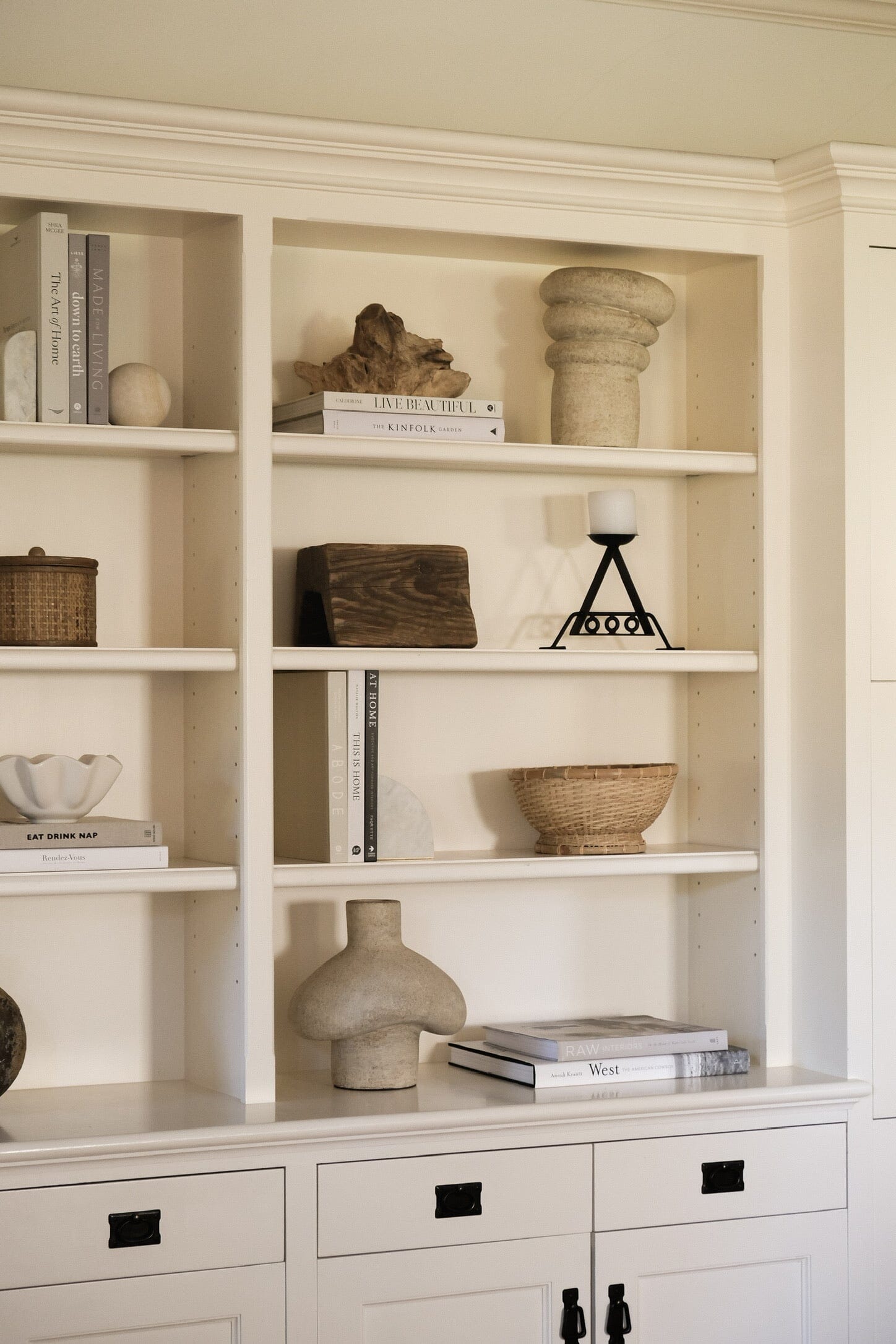 Tanah cream vessel styled among books and decor on a white built in shelf