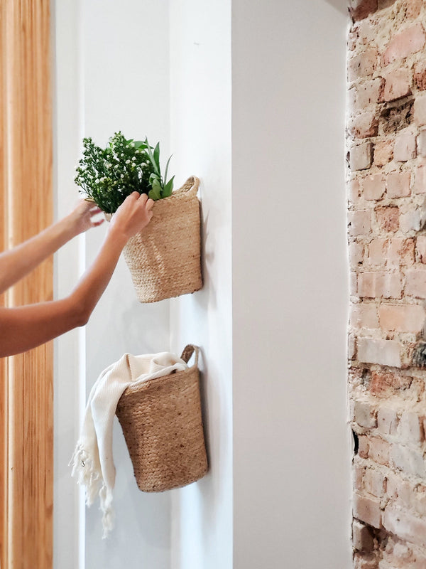 Person placing the kata hand woven basket with greenery against a white wall.