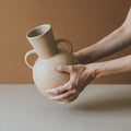 Hands holding the two-handled Tirreno terracotta vase showing its raw matte clay surface