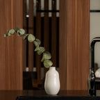 White Gharyan stoneware bud vase holding a eucalyptus stem on a dark counter