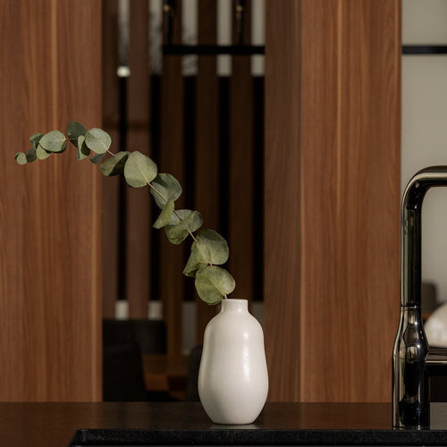 White Gharyan stoneware bud vase holding a eucalyptus stem on a dark counter