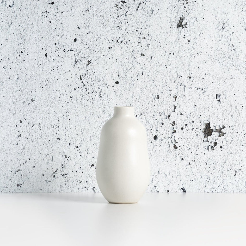 White matte stoneware bud vase against a speckled gray background