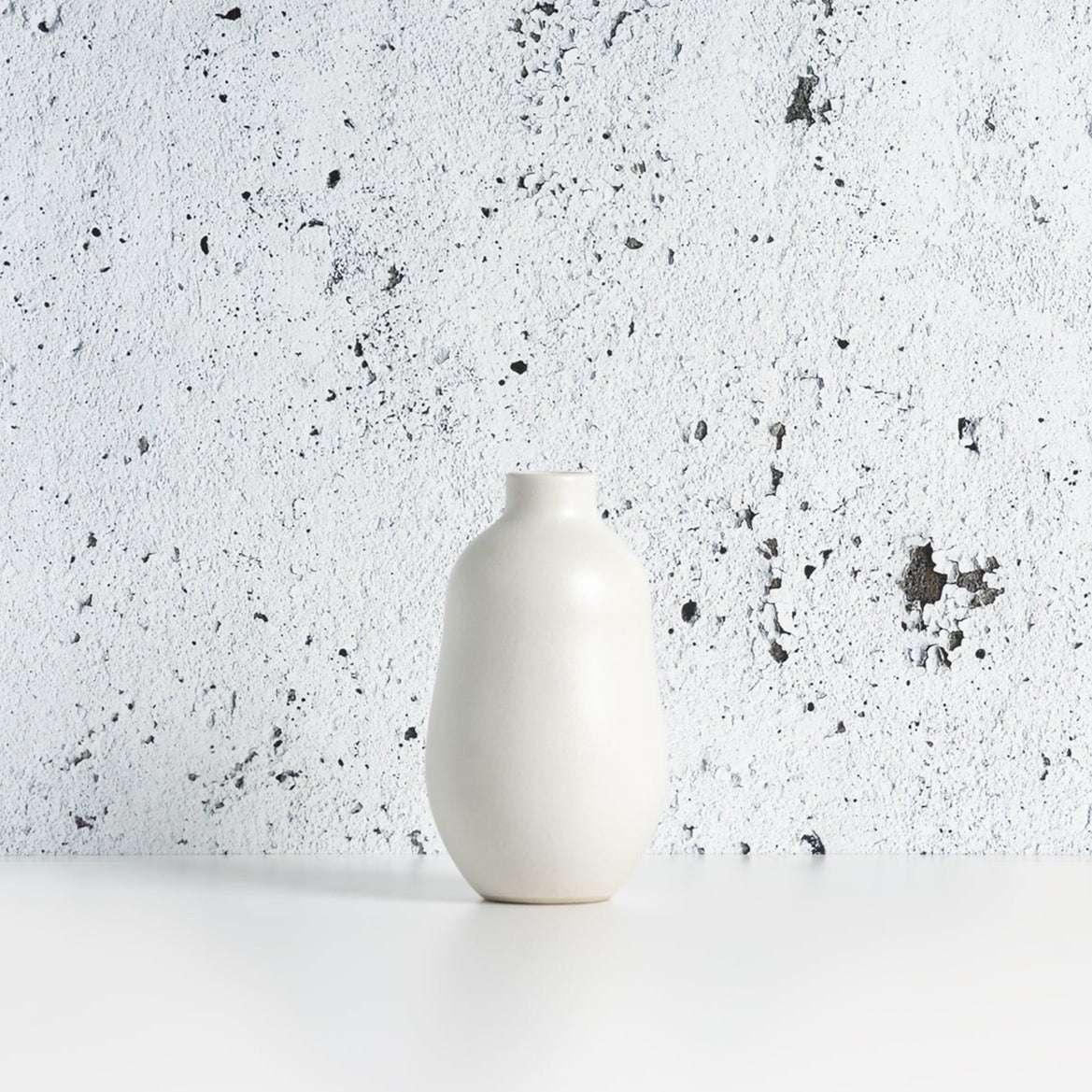 White matte stoneware bud vase against a speckled gray background