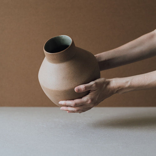 Hands cradling a handmade terracotta vase showing its raw clay surface
