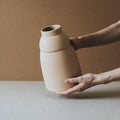 Hands holding the rounded Chubby terracotta vase showing its raw matte clay surface