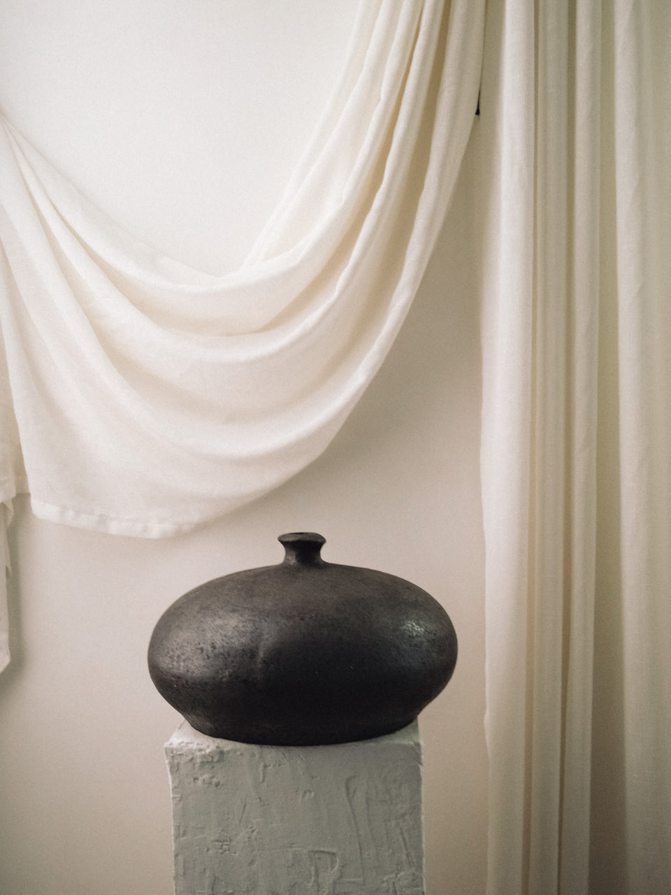  Dark sculptural moon vase with small flat-top neck against a draped curtain